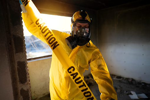 Man in protective workwear putting Caution cordon tape at the ruined building.