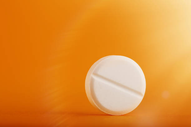 istock White round medical pill on yellow / orange background 1217646201