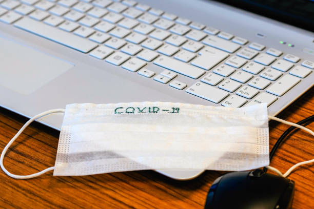 The top view of the workspace during the covid19 (coronavirus) is spreading with a laptop computer, nose mask, glasses, and a cup of herbal drink on a gray wooden table.The idea for coping and virus la vista superior del espacio de trabajo durante el covid19 (coronavirus) se está extendiendo con un ordenador portátil, máscara nasal, vasos y una taza de bebida de hierbas sobre una mesa de madera gris. la idea de la afrontación y el virus