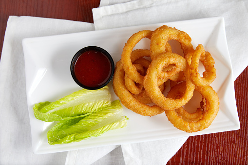 A plate of hot and crisp fried onion rings ready to dip into a side of ketchup