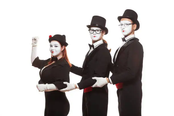 Portrait of three mime artists performing, isolated on white background. Mimes stand and hold on to each other. Symbol of leadership, co-working, team.