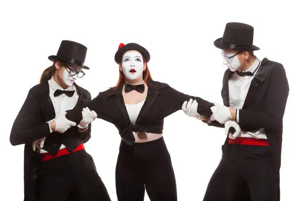 Portrait of three mime artists performing, isolated on white background. Two men pull the girl to sides, can not divide girl. Symbol of rivalry, unrequited love.