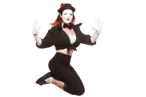 Portrait of female mime artist performing, isolated on white background. Woman jumps very high smiling.