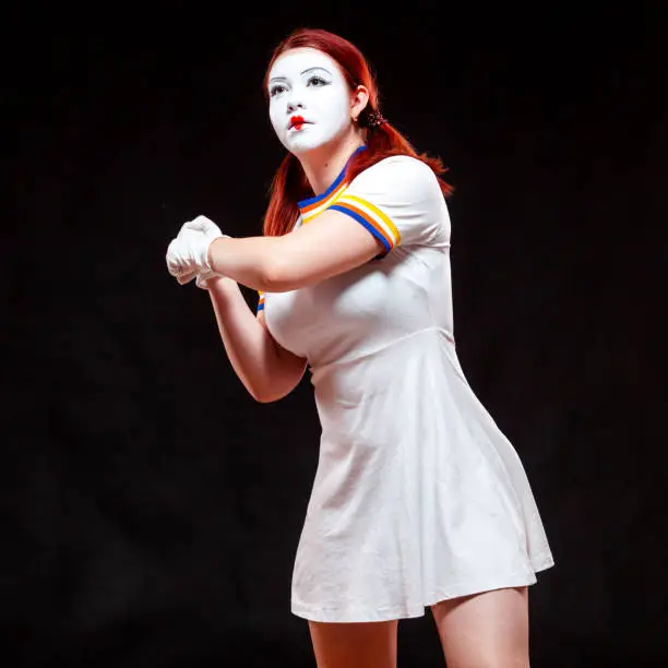 Portrait of female mime artist, isolated on black background. Young woman pretends playing tennis, holding the racket, ready to hit.