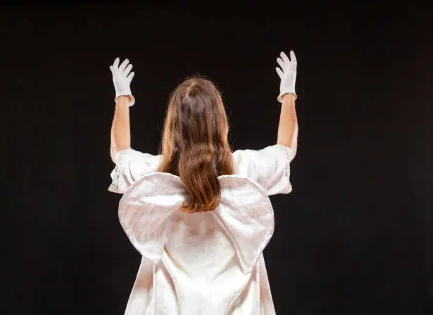 Portrait of male mime artist, isolated on black background. Back view of a man dressed like an angel standing with his hands risen. Symbol of invoke, plead, pray.