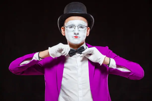 Portrait of male mime artist, isolated on black background. Close up of mans face. Man adjusts his bow tie.