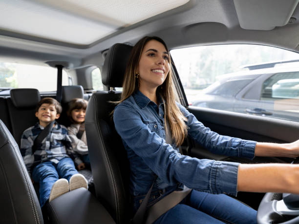 Happy mother riding with her kids in the car Happy Latin American mother riding in the car with her kids and smiling while wearing their seatbelts family in car stock pictures, royalty-free photos & images