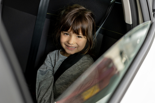 Portrait of a happy girl in a car with her seatbelt on ready to go for a drive and looking at the camera smiling