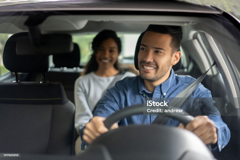 Happy driver transporting a woman in a car Happy Latin American driver transporting a woman in a car while talking to her - transportation concepts Crowdsourced Taxi Stock Photo