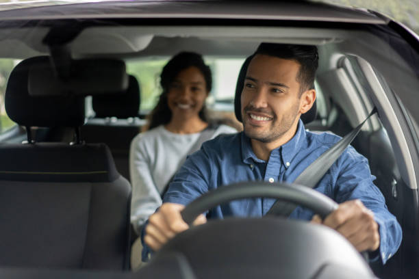 Happy driver transporting a woman in a car Happy Latin American driver transporting a woman in a car while talking to her - transportation concepts driving stock pictures, royalty-free photos & images