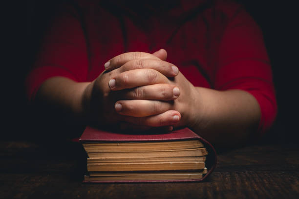 Woman with closed hands on holy bible staying at home and praying for protection ageainst coronavirus covid-19 pandemi concept.