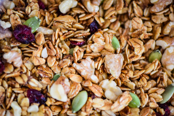 A full frame close-up image of golden brown toasted granola cereal with rolled oats, walnuts, dried cranberries and green pumpkin seeds.