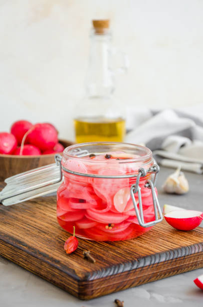 Fermented food. Marinated radish with onion, garlic and spices in a jar on a cutting board on a dark concrete background. Vertical orientation. Copy space