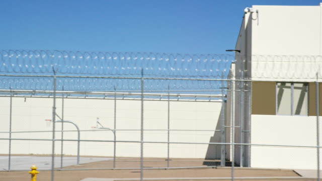 Moving Shot of a Prison in Phoenix, Arizona with a Barbed Wire Chainlink Fence Surrounding an Outdoors Basketball Court on a Sunny Morning