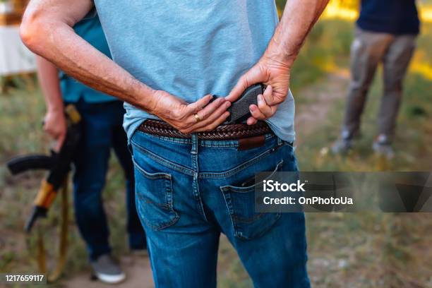 Man Hides A Pistol Behind His Back Under The Belt Of Jeans Stock Photo - Download Image Now