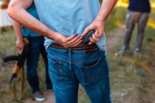 man hides a pistol behind his back under the belt of jeans - waistband imagens e fotografias de stock
