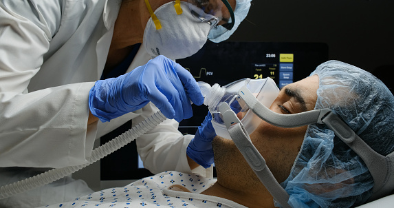 Female caucasian doctor checking on Covid-19 infected patient while connected to a ventilator at a hospital room