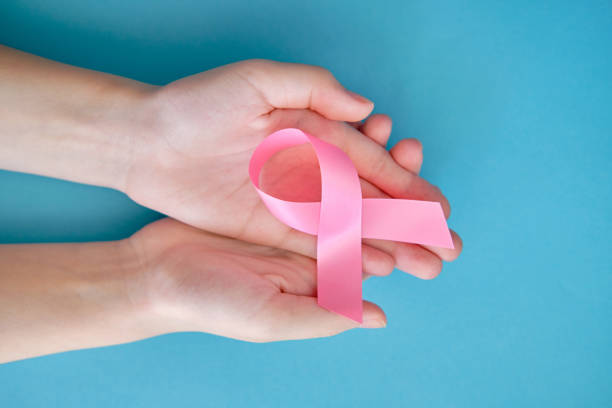 розовая лента на женской руке и синем фоне. рак молочной железы концепция символическая лента - breast cancer pink ribbon alertness стоковые фото и изображения