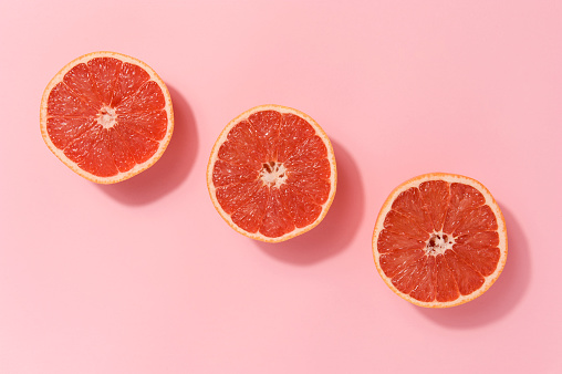 Fresh cut slices of ruby red grapefruit arranged on a pink colored background