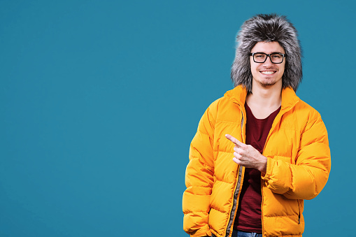 Portrait of happy young man in warm clothing on color background. Ready for winter vacation