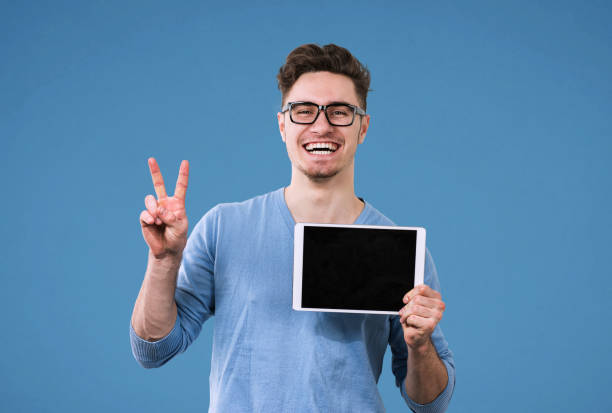 Happy hipster man in glasses with tablet computer giving victory sign