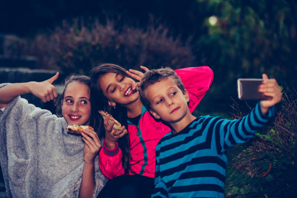 istock Group of a three children taking selfie by smart phone while eating pizza outdoors and showing gesture thumbs up. 1217673905