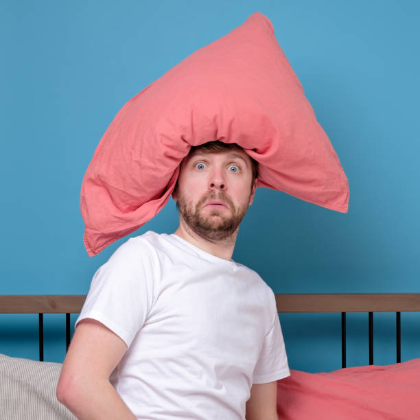 istock Cauacsian young man with pillow on head lying in bed and screaming being alone stressed because of quarantine 1217681377