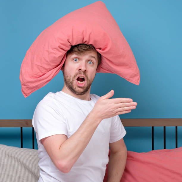 istock Cauacsian young man with pillow on head lying in bed and screaming being alone stressed because of quarantine 1217681391