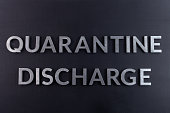 the words quarantine discharge laid with silver metal letters on matte back flat surface directly above in flat lay perspective