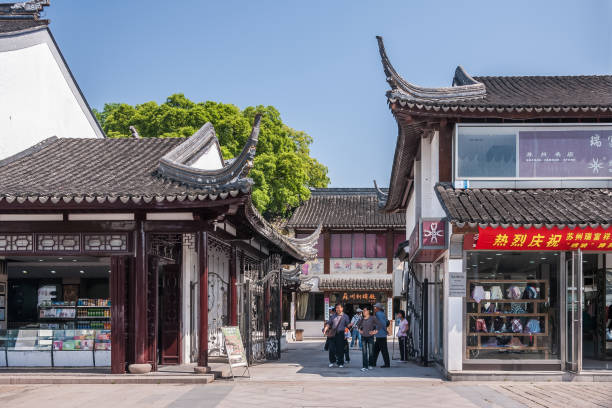 Shopping street in traditional archtecture, Suzhou, China. Suzhou China - May 3, 2010: Shopping street with low white and gray traditional buildings as small shops. Pedestrians walking. Green foliage and blue sky. lake tai stock pictures, royalty-free photos & images