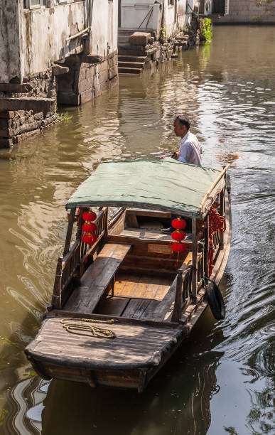 Closeup of brown wooden boat taxi on canal, Suzhou, China. Suzhou China - May 3, 2010: Closeup of brown wooden taxi sloop with red lantern and captain on brown water canal along backside of houses with stairway. lake tai stock pictures, royalty-free photos & images