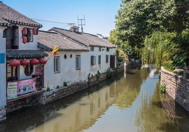 Canal with restaurant and houses and trees, Suzhou, China. Suzhou China - May 3, 2010: City canal reflects white back side of houses and restaurant with red lanterns. Green foliage of trees on other side under light blue sky. lake tai stock pictures, royalty-free photos & images