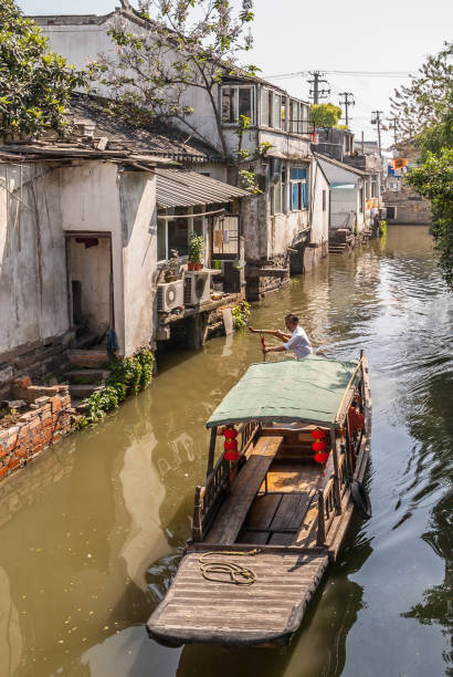 Brown wooden boat taxi on canal, Suzhou, China. Suzhou China - May 3, 2010: Brown wooden taxi sloop with red lantern and captain on brown water canal along backside of houses with stairway. lake tai stock pictures, royalty-free photos & images