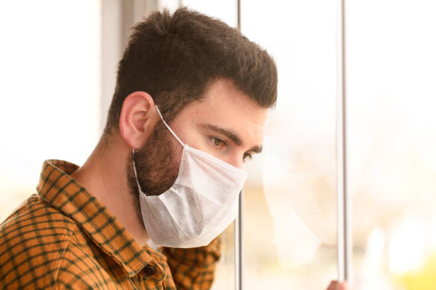 istock Man wearing a protective medical mask looking out of the window during quarantine 1217687424