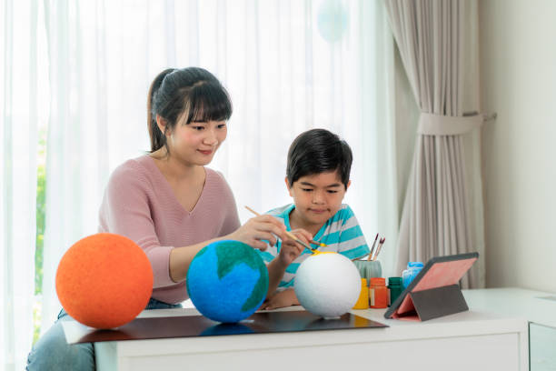 istock Asian elementary schoolboy with mother painting the moon in science class learning about the solar system via video conference with teacher and other classmates at home, Homeschooling and distance learning. 1217687574