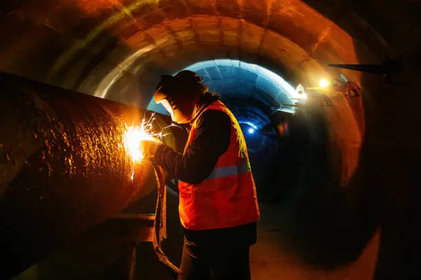 Photo of Worker in protective mask welding pipe in tunnel