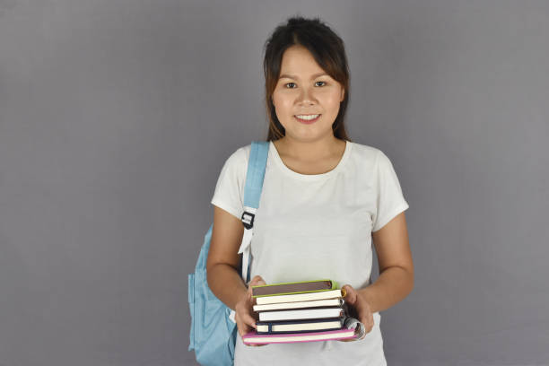 istock asian beautiful young student smiling with backpack and holding books on gray background with copy space. 1217688584