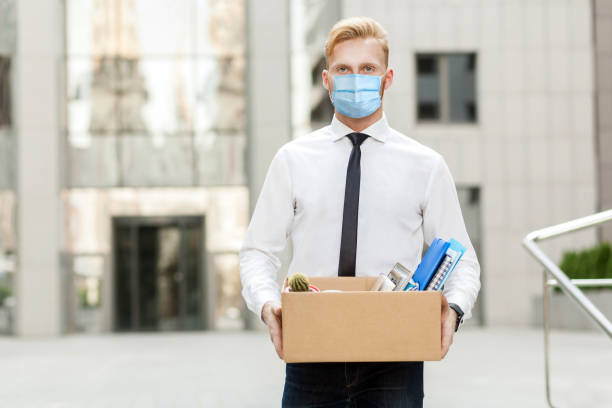 lose job, Youre fired. Unhappy business man with surgical medical mask going out with cardboard, looking at camera and feeling looser. lose job, Youre fired. Unhappy business man with surgical medical mask going out with cardboard, looking at camera and feeling looser. Outdoor shot. business, working and health care concept. demobilization photos stock pictures, royalty-free photos & images