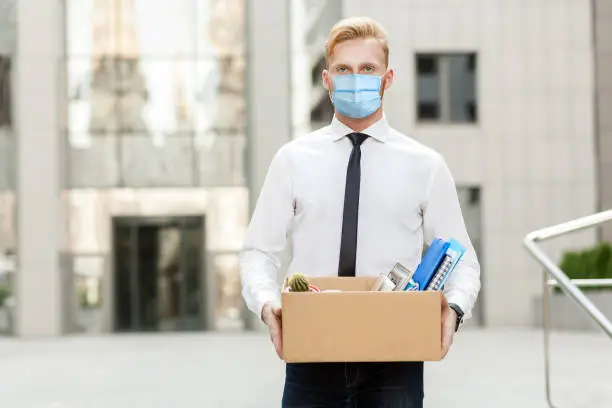 Photo of lose job, Youre fired. Unhappy business man with surgical medical mask going out with cardboard, looking at camera and feeling looser.