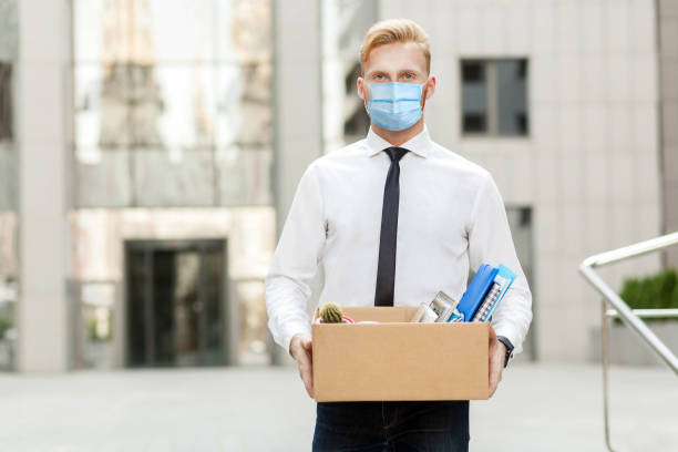 perder o emprego, você é demitido. homem de negócios infeliz com máscara médica cirúrgica saindo com papelão, olhando para a câmera e se sentindo mais solto. - finishing employment issues occupation downsizing - fotografias e filmes do acervo