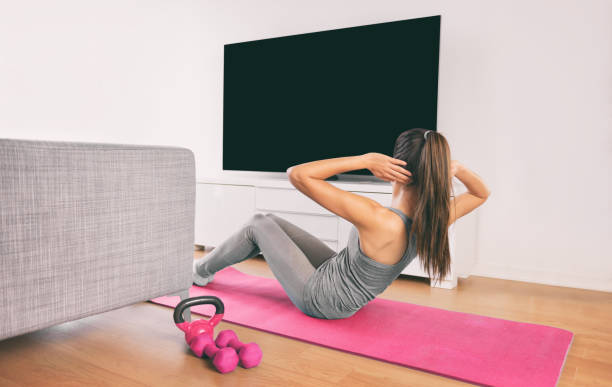 筋力トレーニングをしているホームフィットネスの女性は、家やアパートのリビングルームでスマートテレビにキャストオンラインライブストリームワークアウトウェブビデオを見て体重の� - living room learning healthy lifestyle one person ストックフォトと画像