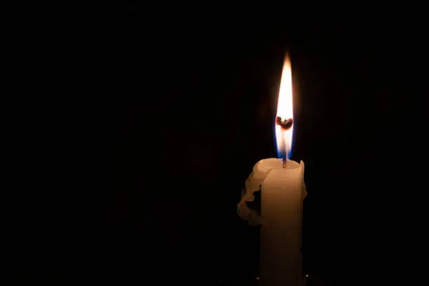 White candle burning on a black background.