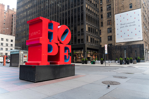 New York City, NY, USA - April 6, 2010: HOPE sculpture by Robert Indiana installed at 7th Avenue and W53 Street of Midtown Manhattan brings hope to New Yorkers' minds and hearts.  Ironically, the name of Chase back, which is closed now due to coronavirus, reflecting on the surface of the sculpture, and 2020 Elections banner in the backdrop added some grief context.