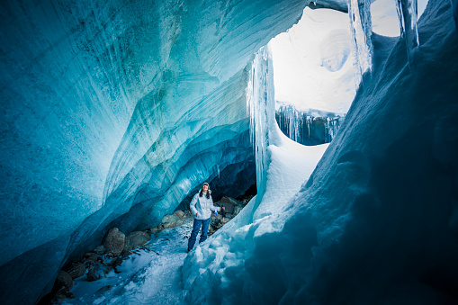 Female explorer wearing ski gear and helmet touching ice in glacial cave.