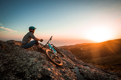 Fit man standing with his mountain bike on top of cliff looking at ocean.