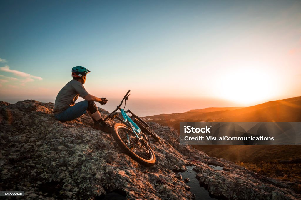 Male athlete mountain biking in Portugal. Fit man standing with his mountain bike on top of cliff looking at ocean. Cycling Stock Photo