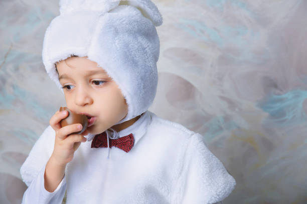 A beautiful little boy in a white Easter Bunny costume. A child with chocolate eggs in his hands. Symbol of Easter holidays with sweets and willow
