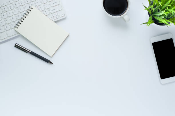 istock Workplace in the office with a white desk. Top view from above of keyboard with notebook and pen. Space for modern creative work of designer. Flat lay with copy space. Business and finance concept. 1217726507