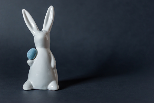 Porcelain white Easter bunny with egg on black background