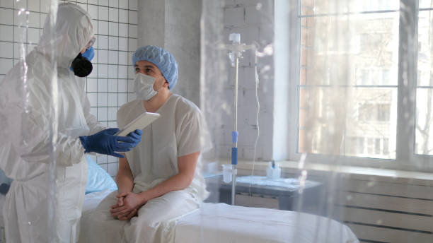 Doctor in protective suit talking with patient showing tablet in